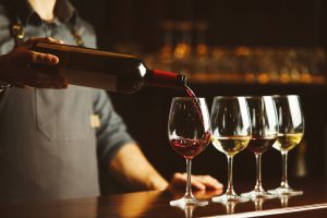 Man at the bar pouring glasses of red wine and white wine