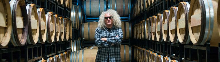 Charles Smith of K Vintners stands confidently in a barrel room, surrounded by aging wine, embodying bold winemaking and rock-and-roll style