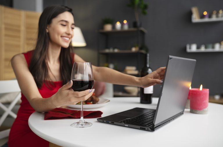 young adult woman enjoying a virtual date, drinking a glass of wine or shopping for wine online